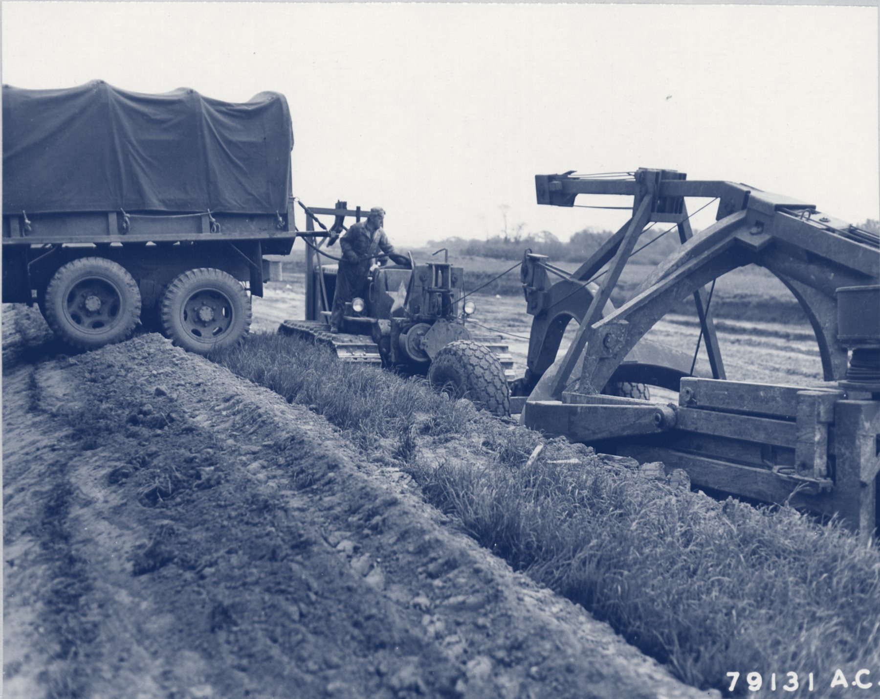 Army tractor, truck, and earth-moving scraper on a muddy field in England