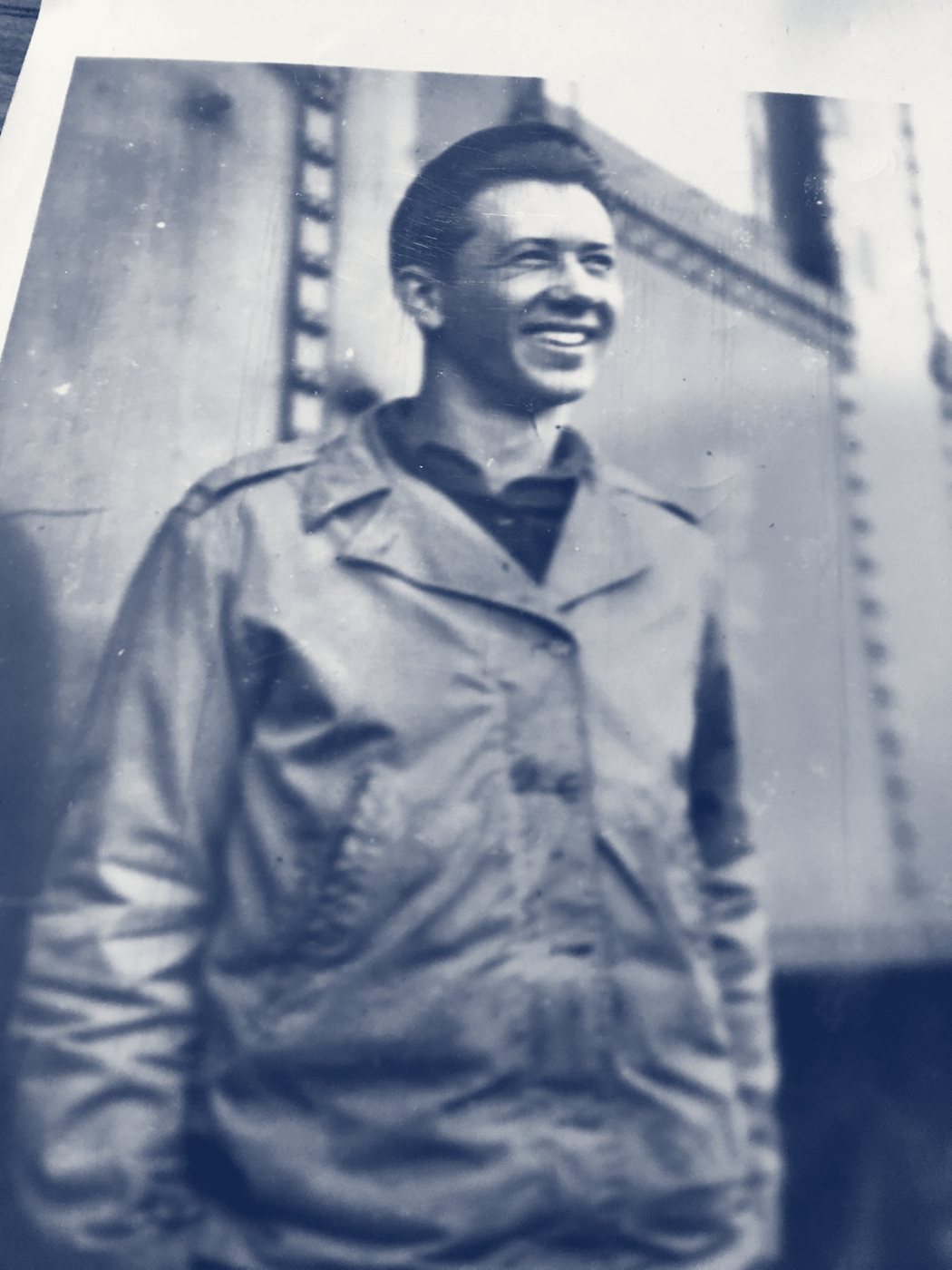 A smiling young soldier in an Army field jacket beside a riveted steel structure