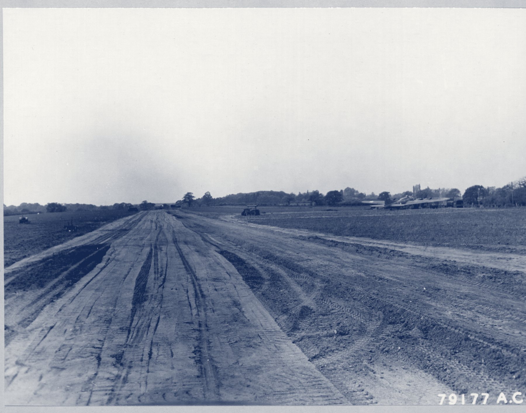 A long, freshly graded dirt runway across a flat English field