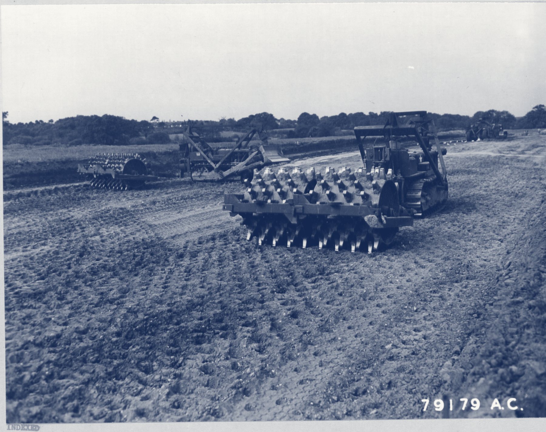 Tractors pulling sheep-foot rollers across a field
